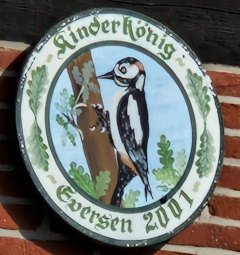 Kinderkönigsscheibe des Schützenvereins Eversen aus dem Jahr 2001: Dargestellt mit einem Buntspecht auf einem Ast, umgeben von einem dekorativen Rahmen und der Inschrift Kinder König Eversen 2001.