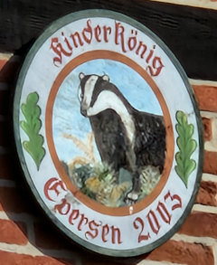 Scheibe des Kinderkönigs des Schützenverein Eversen im Jahr 2003: Dargestellt mit einem Dachs in natürlicher Umgebung, umgeben von Eichenblättern und der Inschrift Kinder König Eversen 2003.