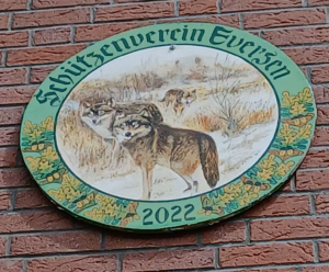 Schützenscheibe des Schützenvereins Eversen aus dem Jahr 2022. Das runde Schild zeigt zwei Wölfe in einer winterlichen Landschaft mit hohem Gras und kahlen Bäumen. Der Rand ist mit grünen Eichenblättern verziert, und oben steht der Vereinsname in gotischer Schrift: 'Schützenverein Eversen'